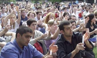 A crowd of people hold candles up outside.