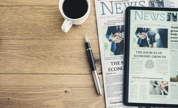 Newspaper and digital tablet on wooden table.