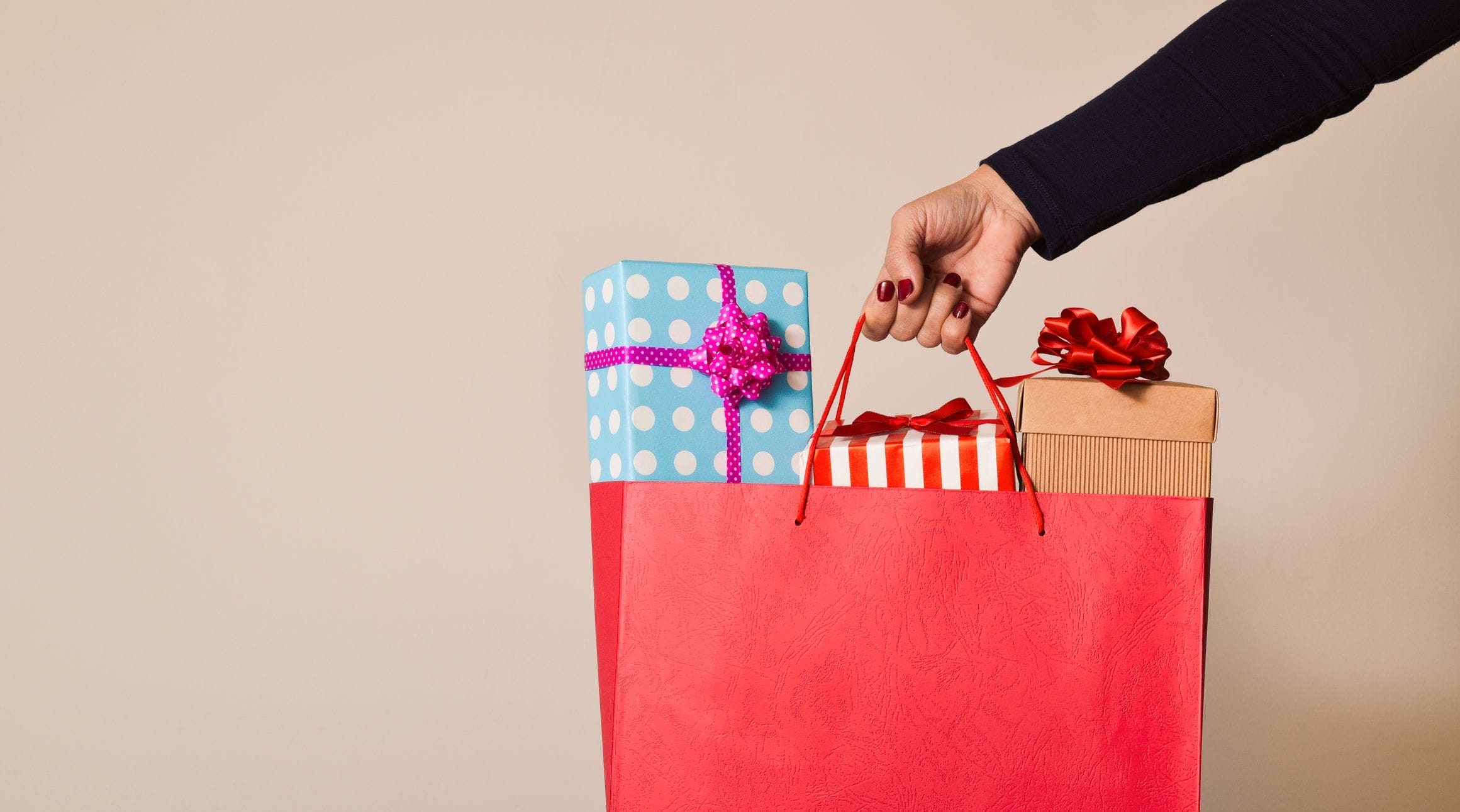 A woman holding a gift bag with three wrapped presents sticking out.