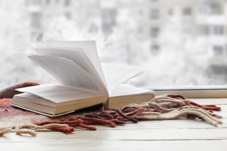 An open book next to a window with snow falling outside.