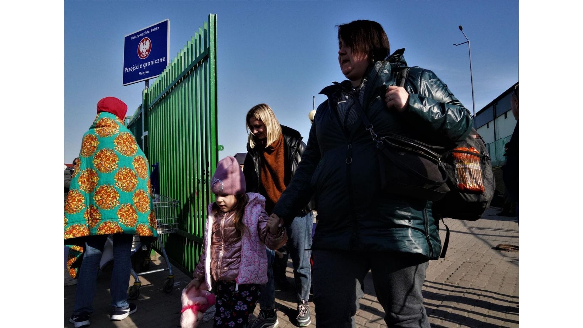 A woman holding a child's hand as they pass through an entry gate on the Ukraine-Poland border.