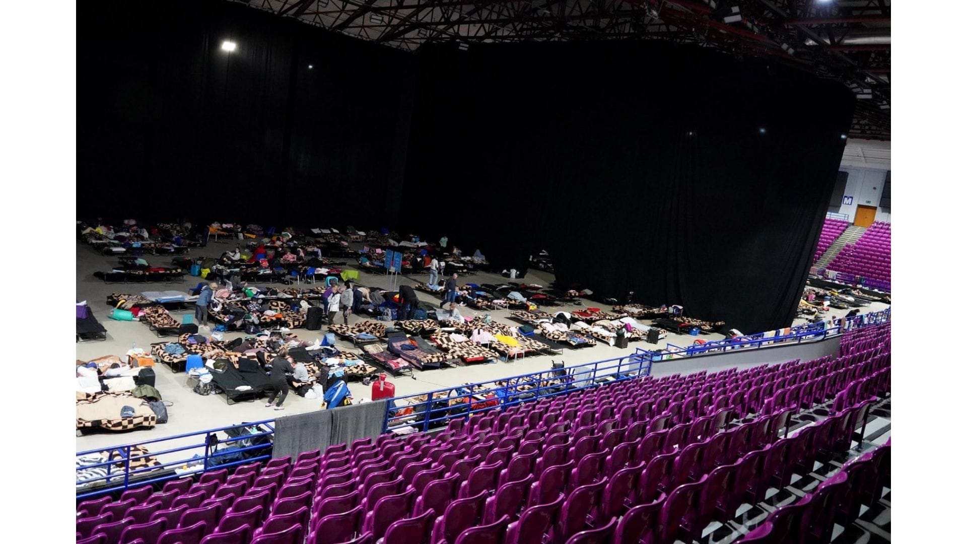 People sleeping on the floor in an arena.