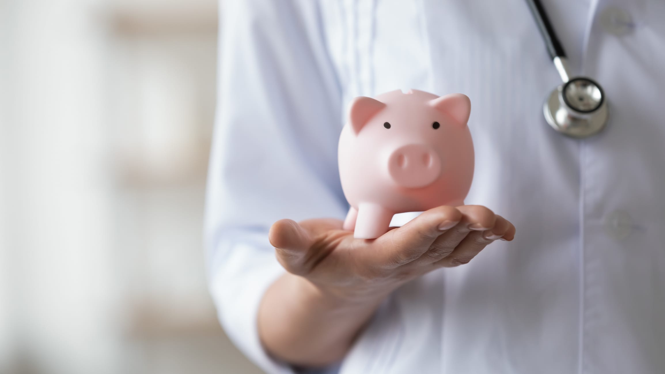 Person wearing a stethoscope and holding a piggy bank