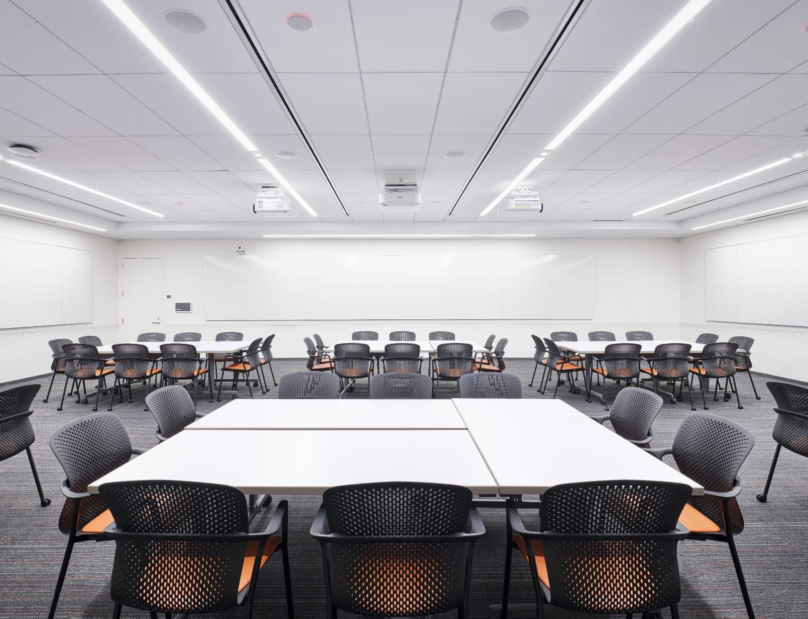 A modern classroom with whiteboards on multiple walls and clusters of moveable and reconfigurable tables and chairs.