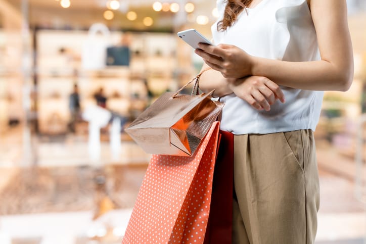 A woman using her smartphone and holding holiday shopping bags.