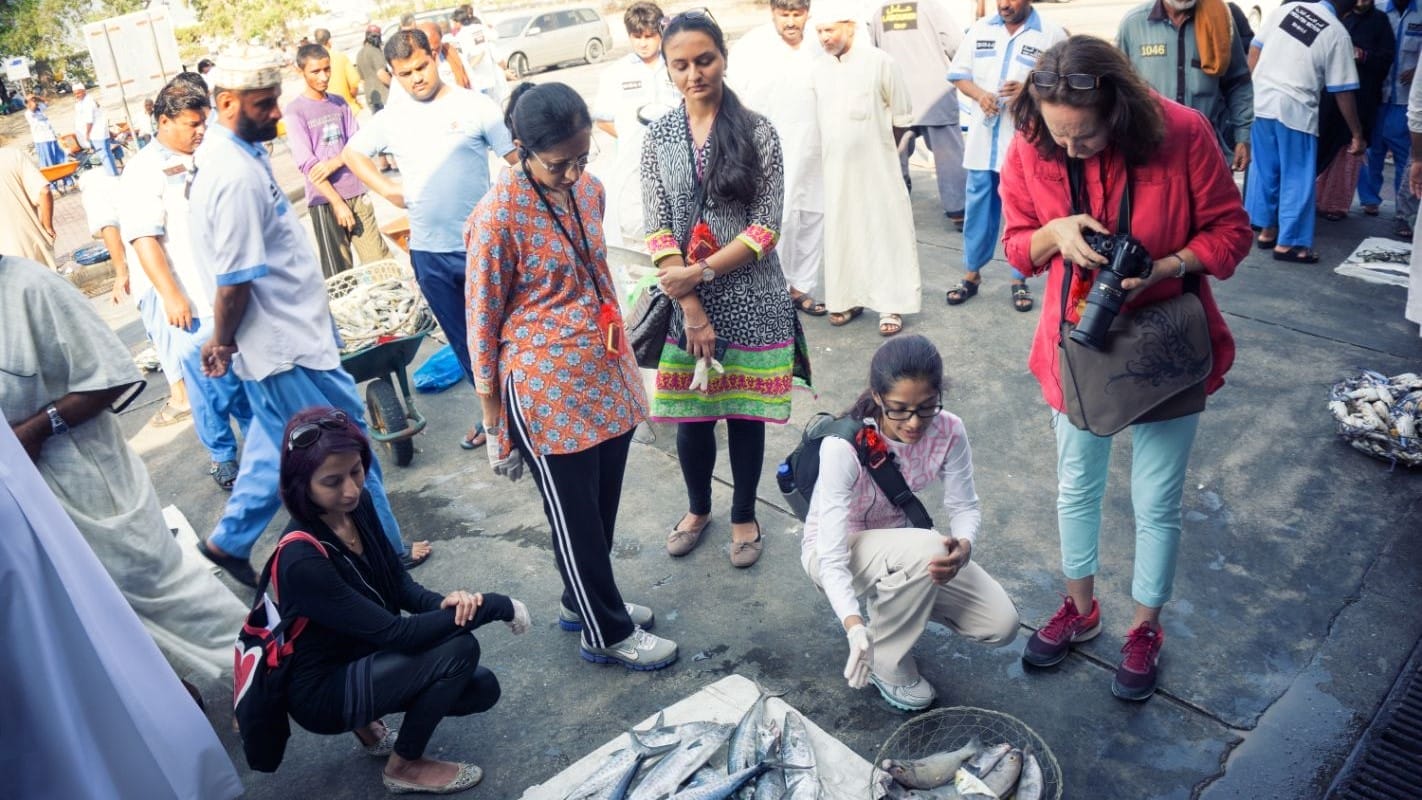 Arva Ahmed kneels in a market to look at fish.