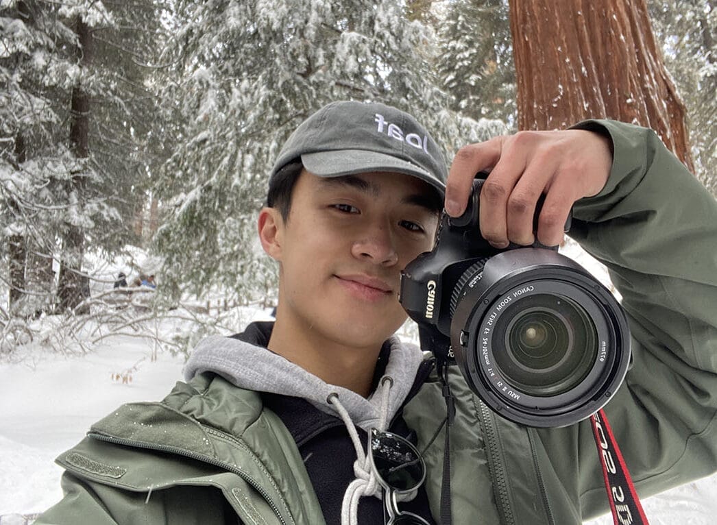 Self-portrait of Jesse Zhang holding a camera among redwood trees in the snow.