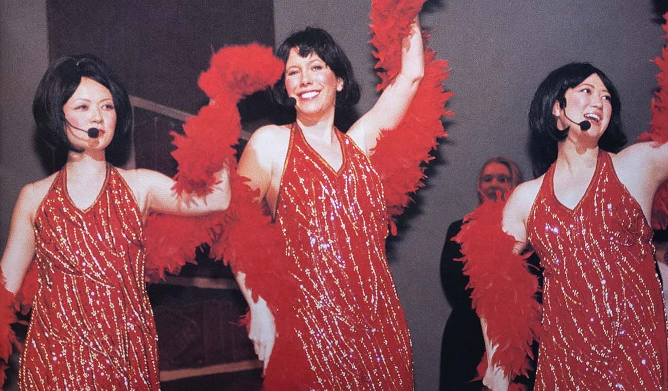 Three women performers in black wigs and red dresses laced with diamonds.