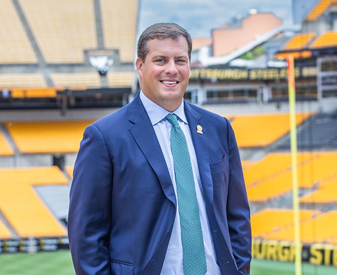 Man in a blue suit posed in the stands of the Pittsburgh Steelers' stadium.