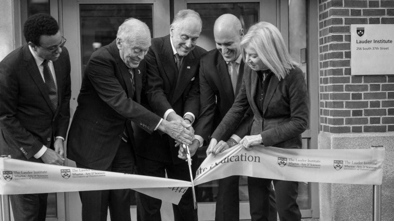 Five people stand in front the entrance to the Lauder Institute cutting a ribbon.