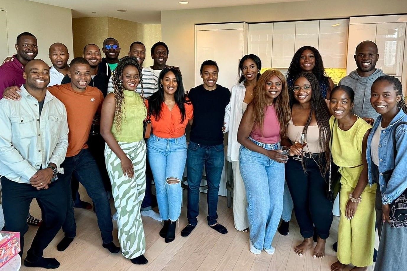 Eighteen students and alumni pose for a photo in someone's home.