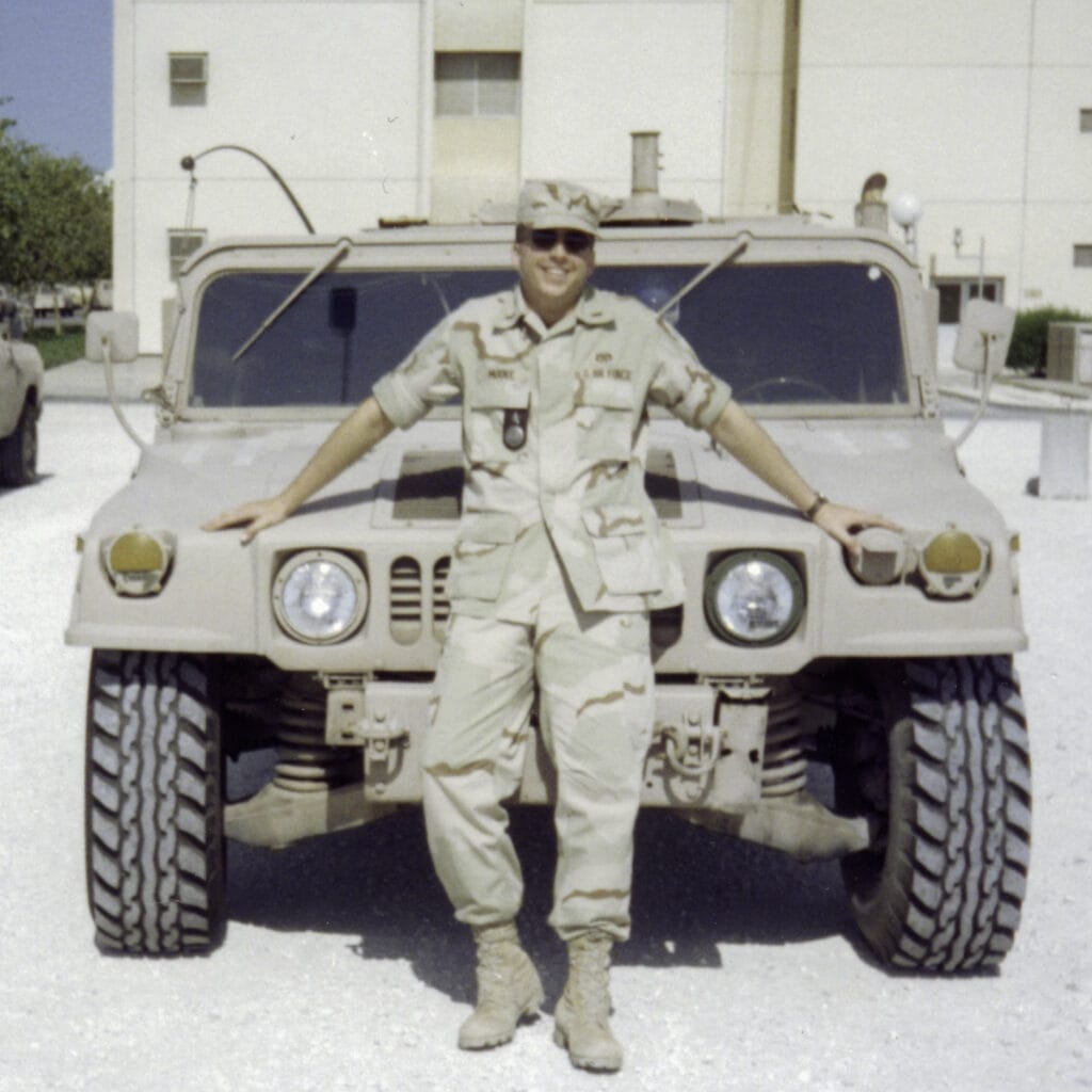 Daniel Moore wearing fatigues in front of a military vehicle.