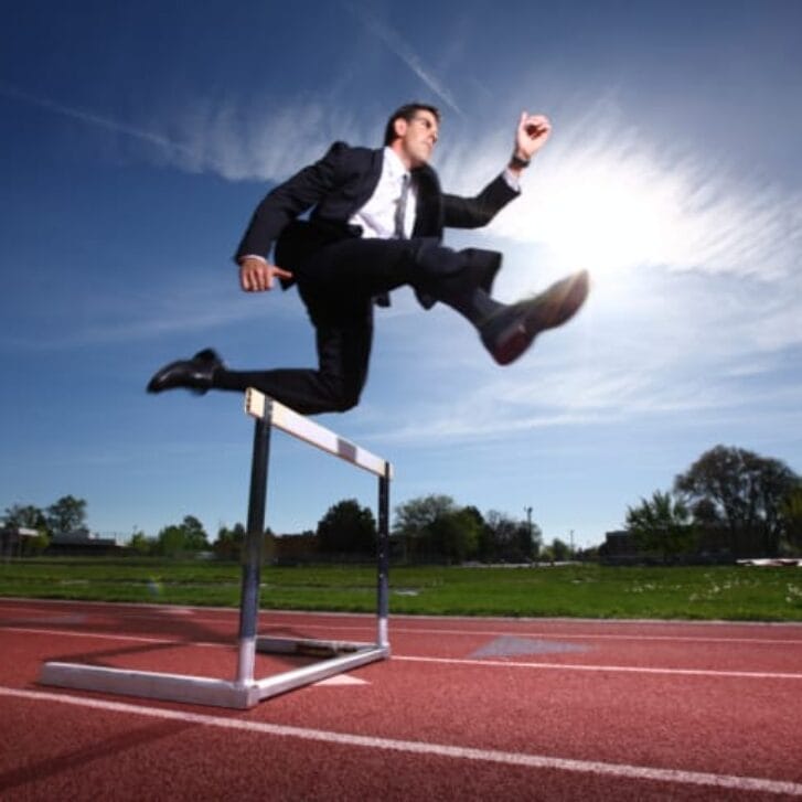 Man in business suit jumping a hurdle
