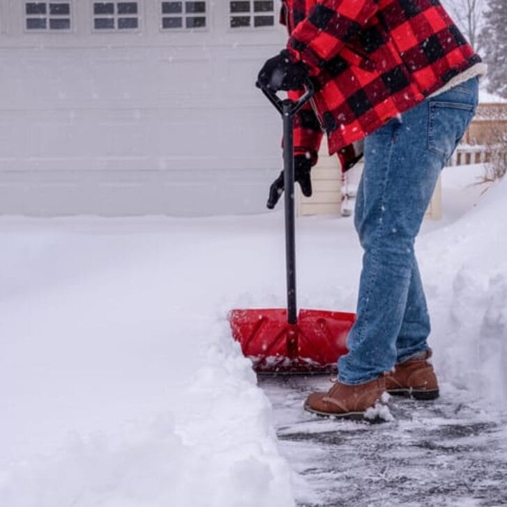 A man shoveling the driveway after a heavy snowfall.