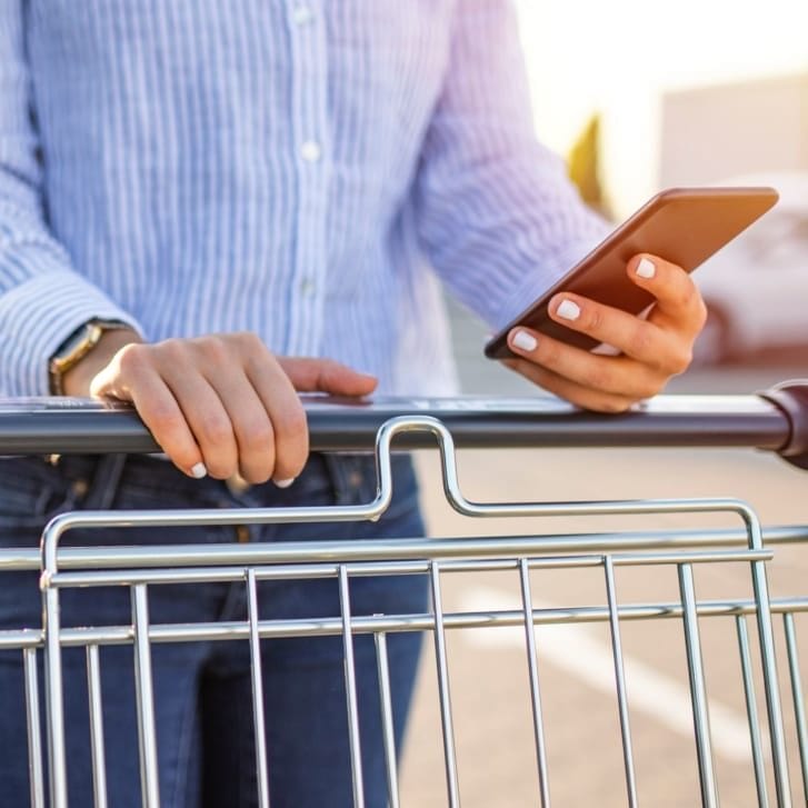 woman steering a shopping cart and looking at cell phone.