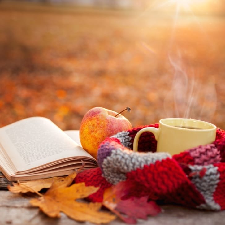 A tea mug, scarf, apple, and book all resting on a table.