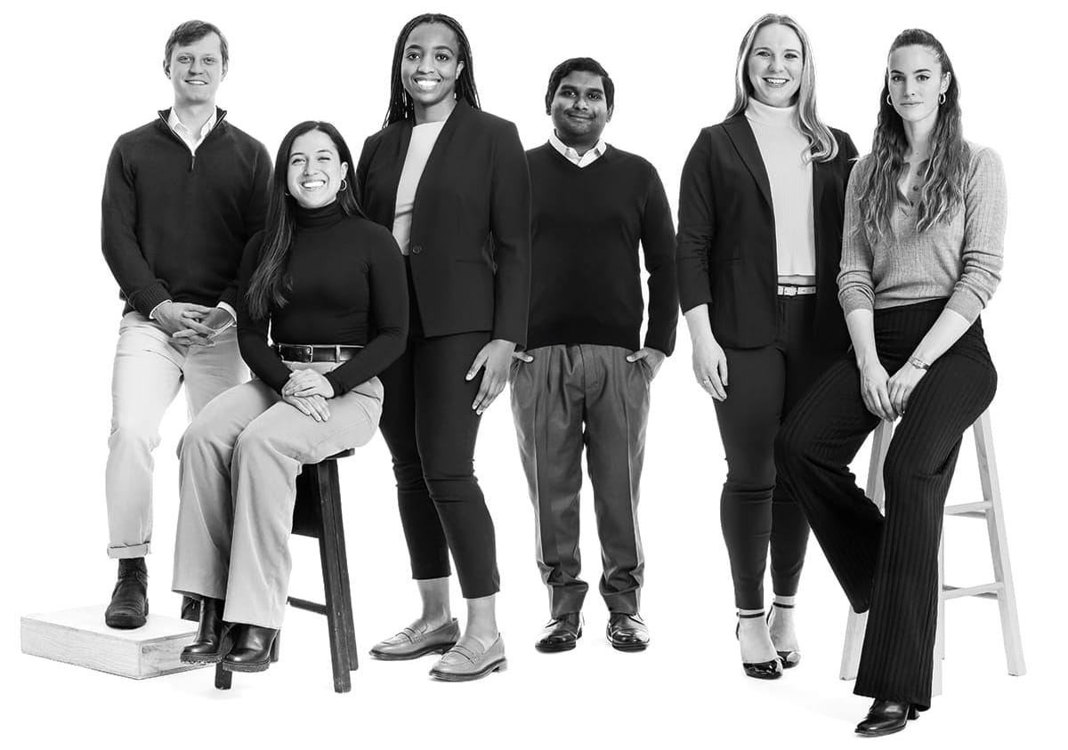 Black and white portrait of six students posed in a studio against a white backdrop with all of them in business casual clothing.