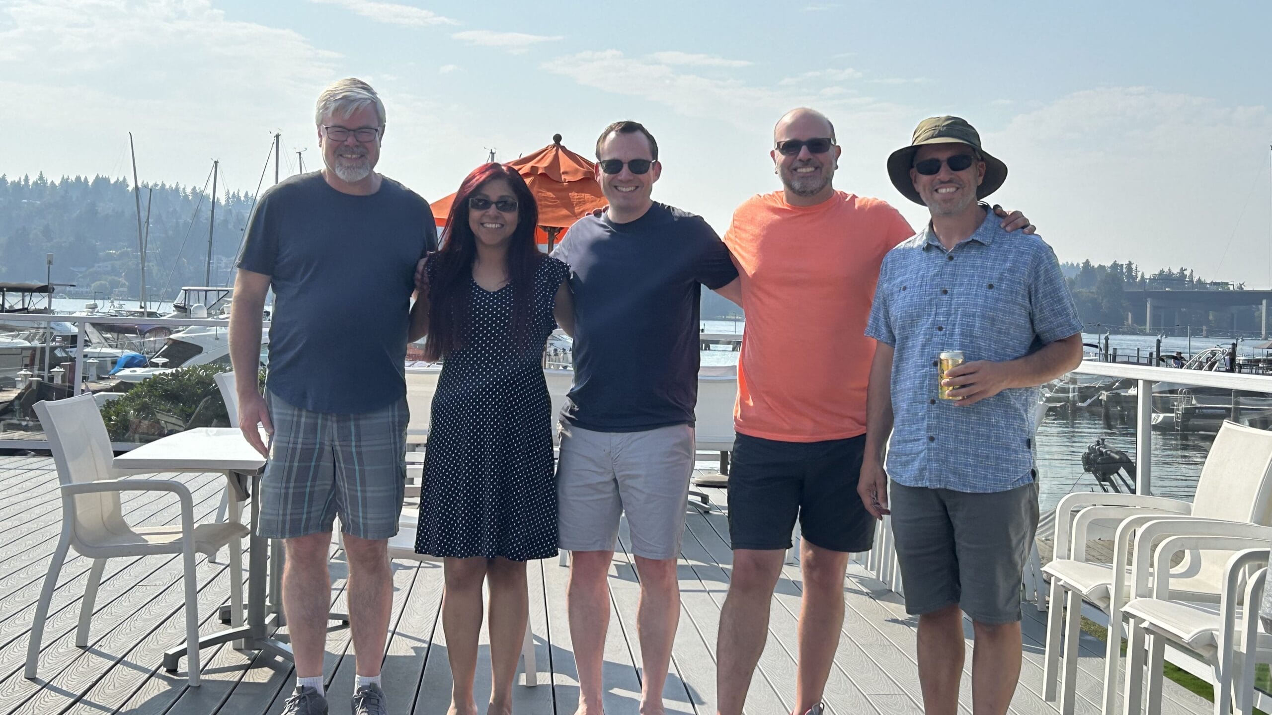 Five people in casual summer clothing stand on a dock together.