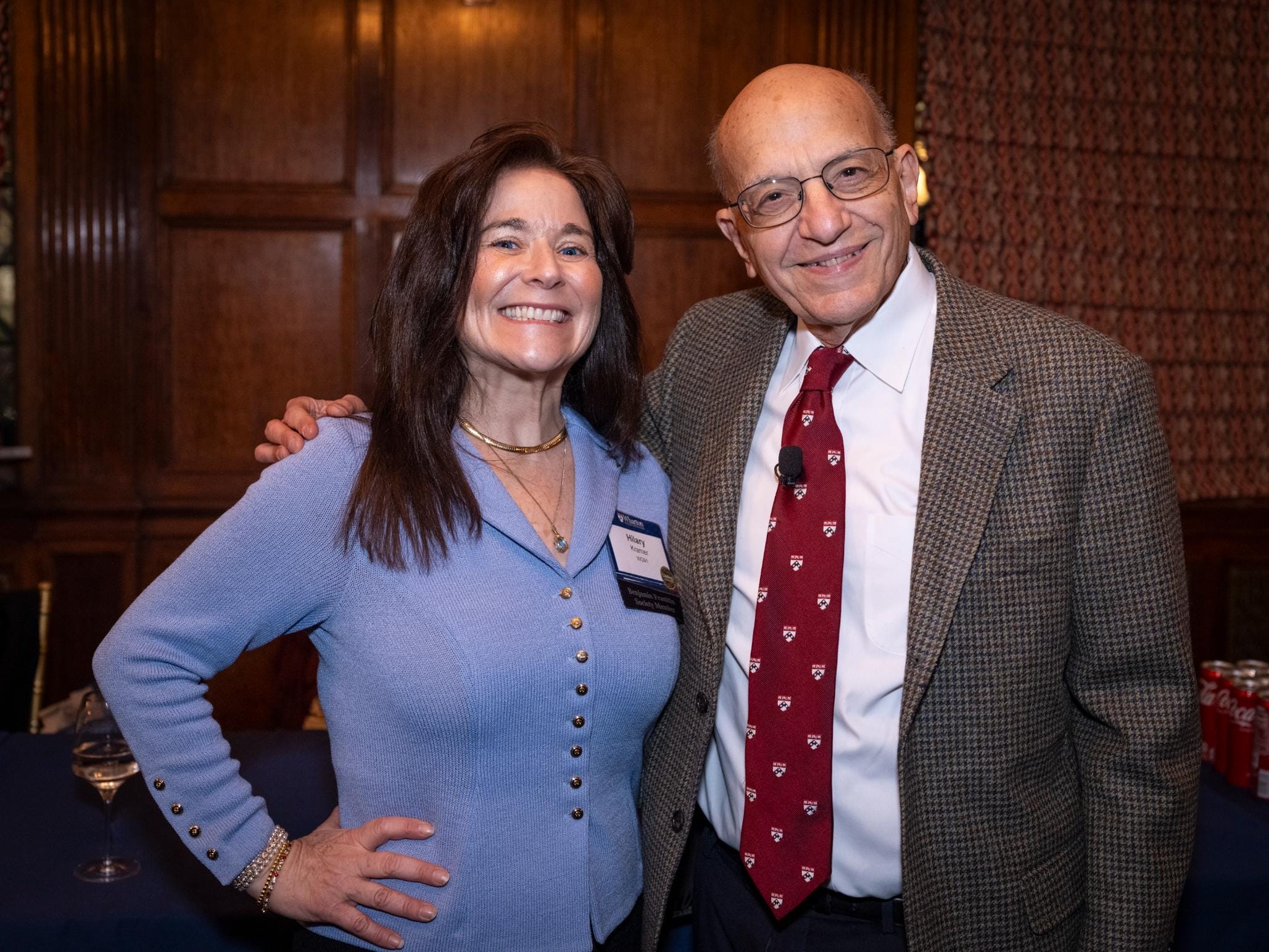 Hilary Kramer in a light blue sweater poses with Jeremy Siegel in a brown suit jacket, white shirt, and red tie with Penn shields on it.