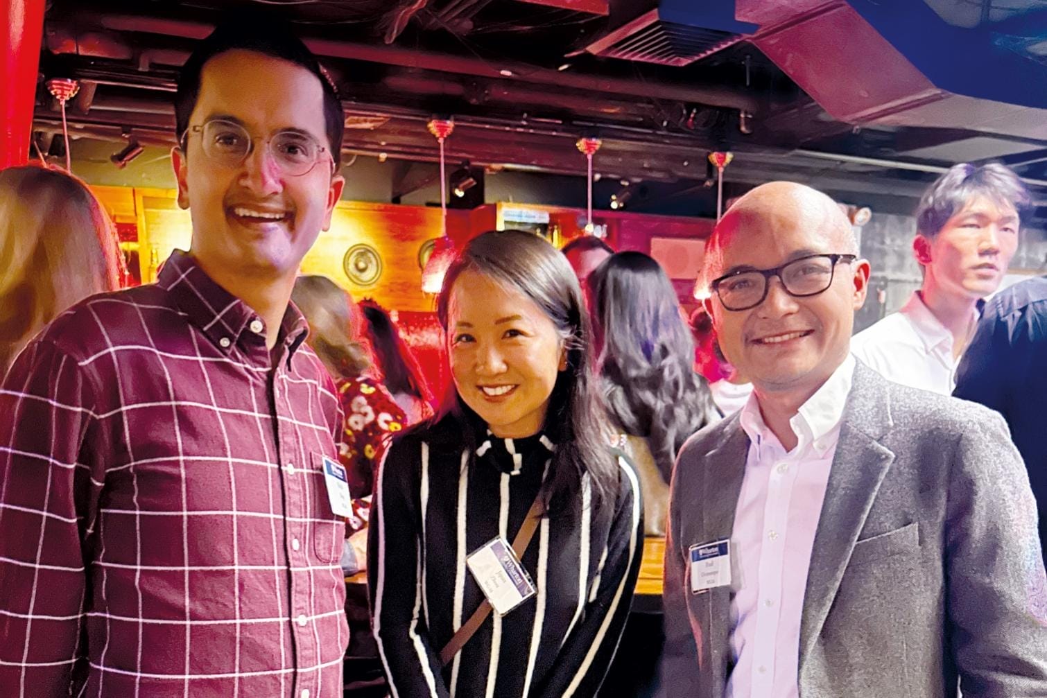 Three people in business casual attire and a casual event space smile for the camera.