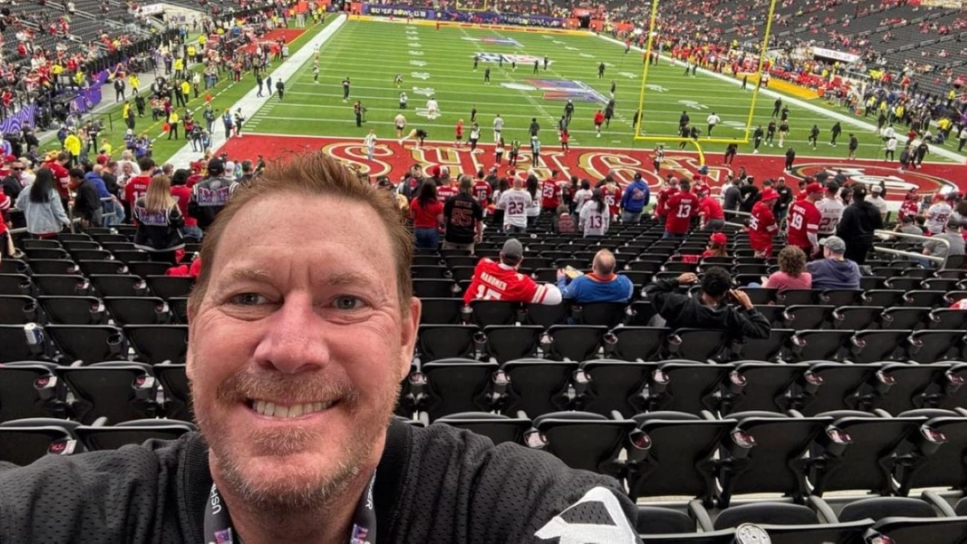 A man in a football jersey takes a selfie in a stadium.