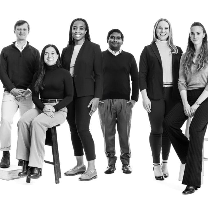 Black and white portrait of six students posed in a studio against a white backdrop with all of them in business casual clothing.