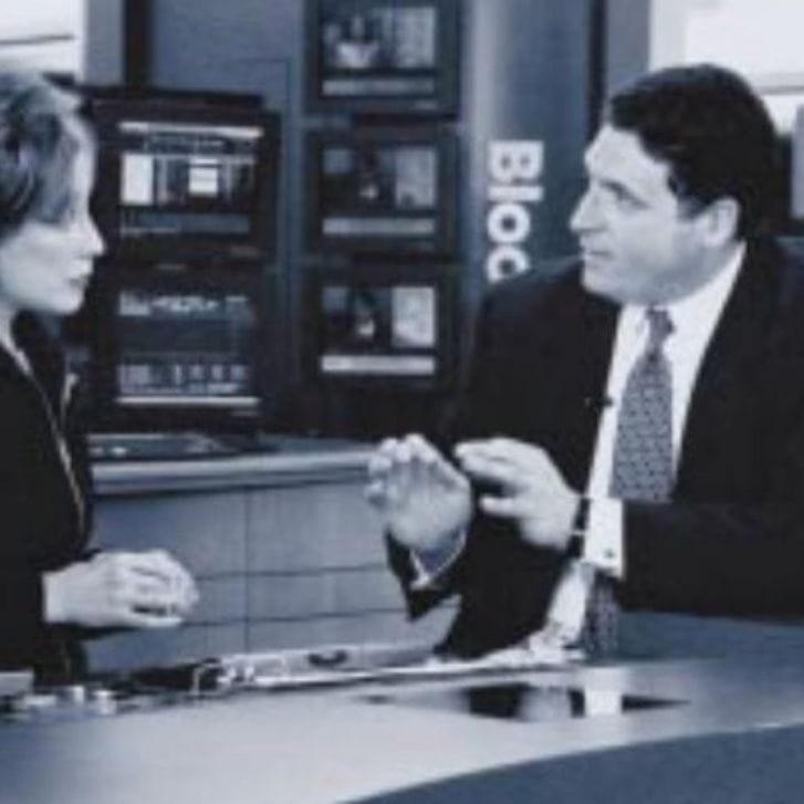 A woman and a man both in business attire speak in front of a Bloomberg news desk