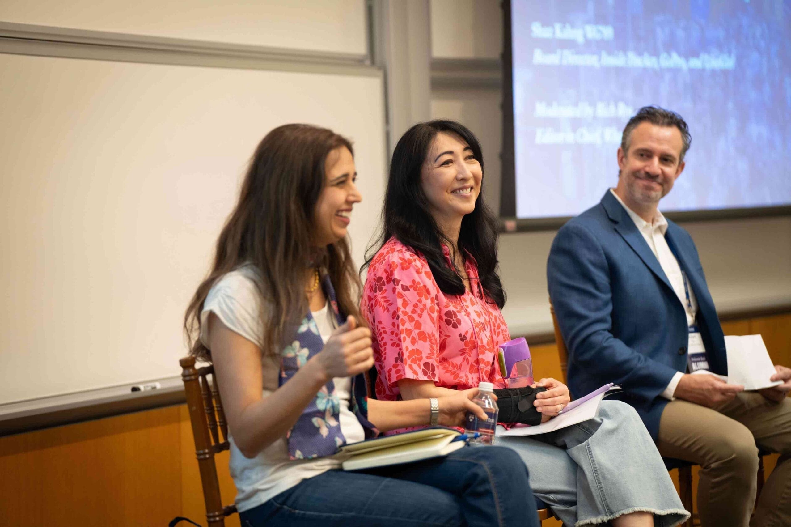 Three people sit at the front of a classroom for a panel session.