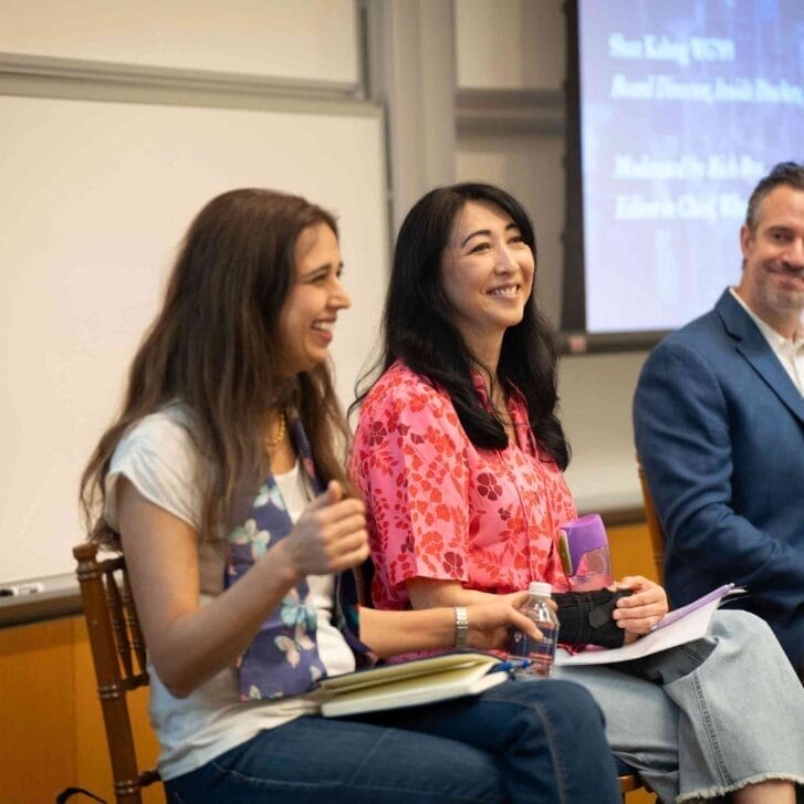 Three people sit at the front of a classroom for a panel session.