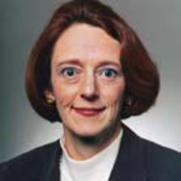 Woman with red hair poses in a white shirt and a blazer.
