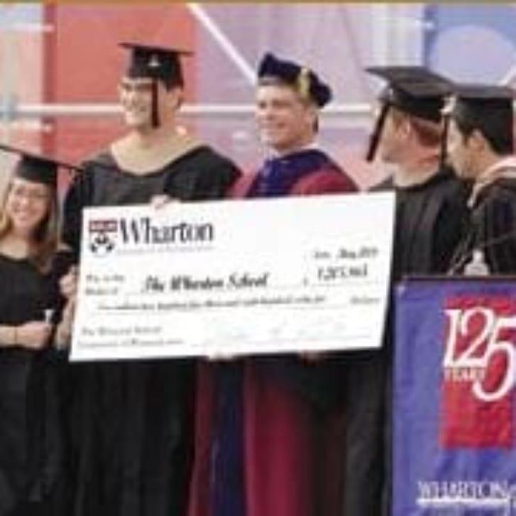 Wharton graduates stand on the ceremony stage in regalia with a check.