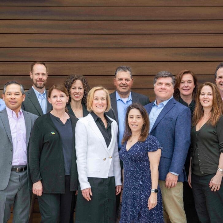 NextAccess partners posing together in front of a wooden planked wall.