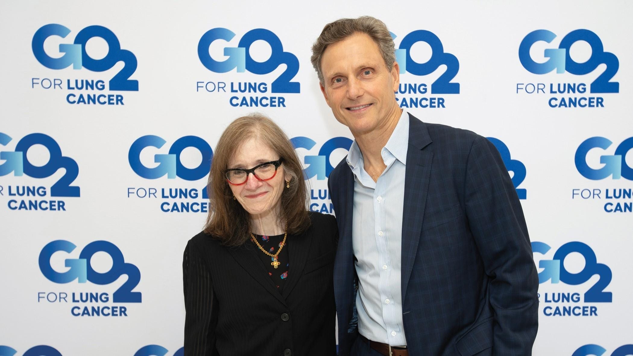 Alumna Adrienne Halper and actor Tony Goldwyn stand in front of a backdrop with the words G02 for Lung Cancer.