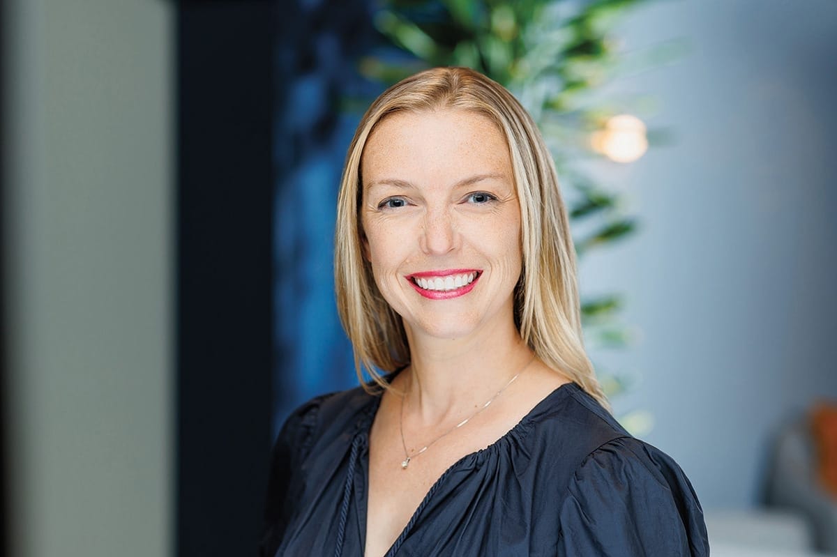 Portrait of a woman with blond hair wearing a silver necklace and a semi-formal blue shirt.