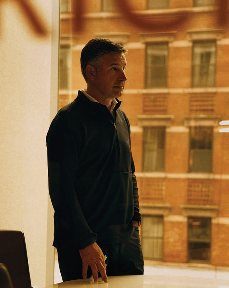 Portrait of Anthony Noto in a quarter-zip shirt standing at a round table with his fingers lightly touching the surface.