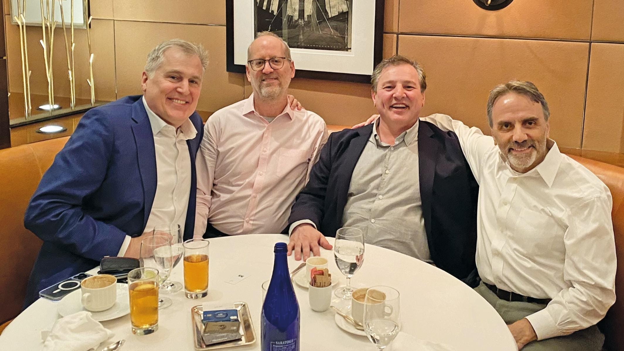 Four alumni in business attire sit around a round table enjoying lunch.