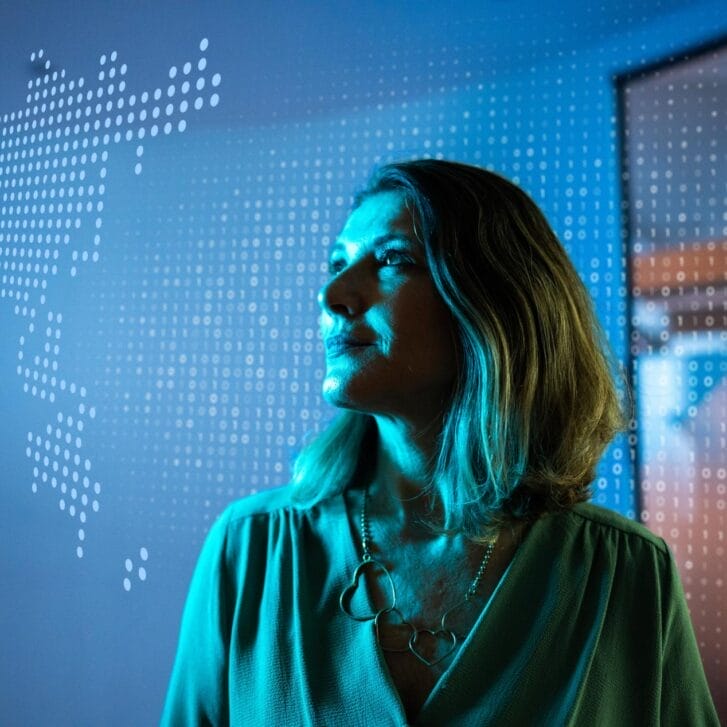 Woman gazing upwards in front of a digitized map of the world.