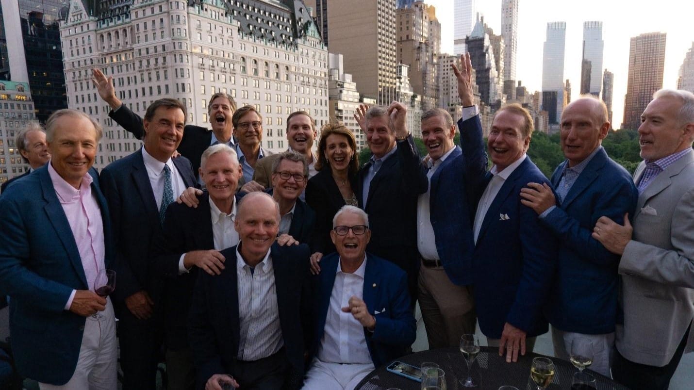 Alumni in suits smiling and cheering for a photo on a New York rooftop.