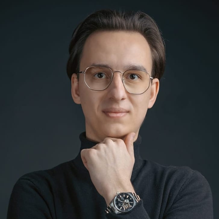 Portrait of a man in a black turtleneck and wire-frame glasses.