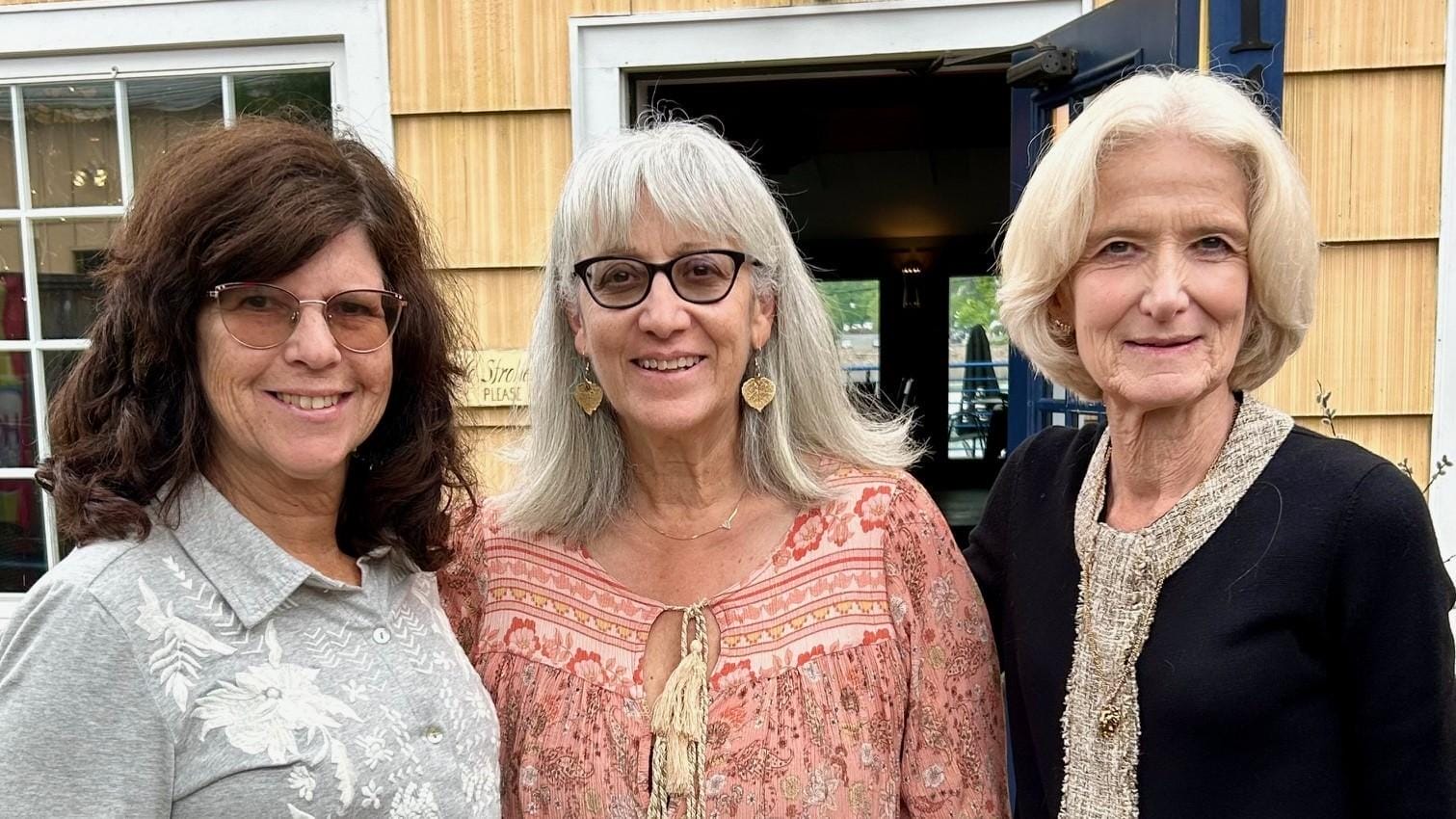 Three alumnae stand outside in front of an entryway.