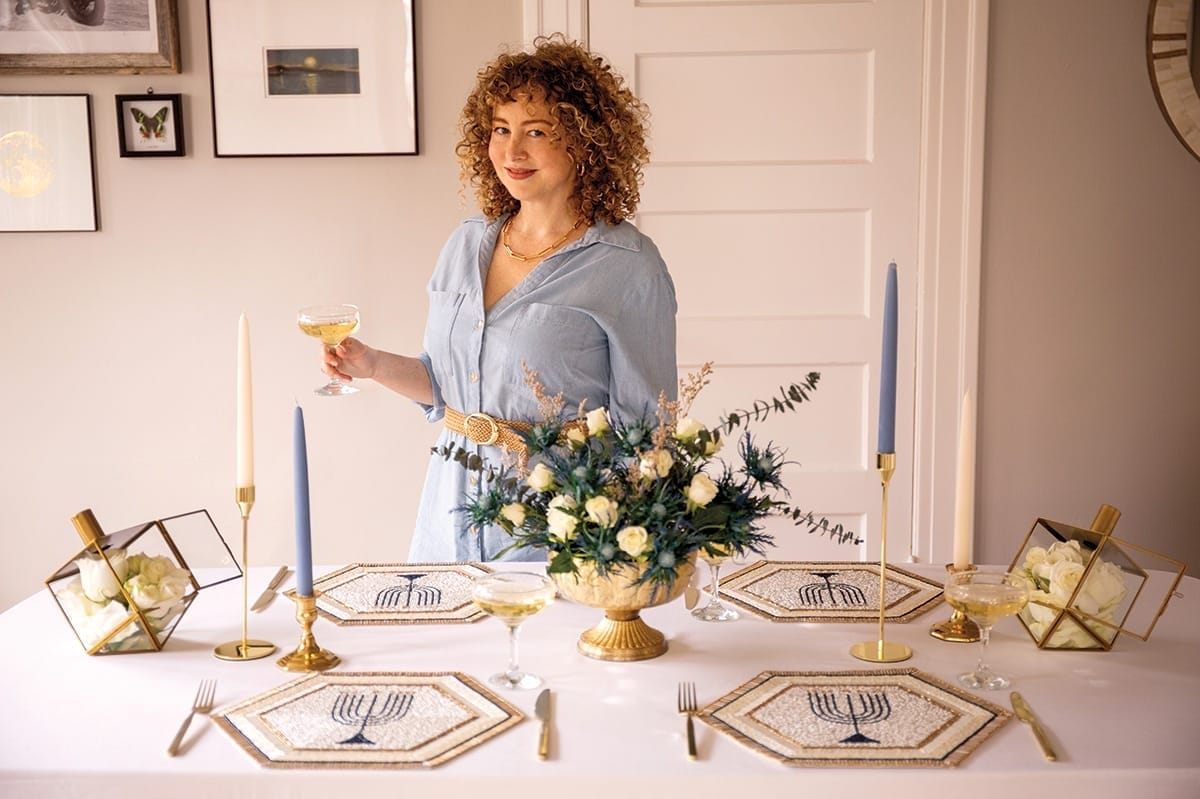 Portrait of a woman standing in front of a table adorned with Jewish decor.