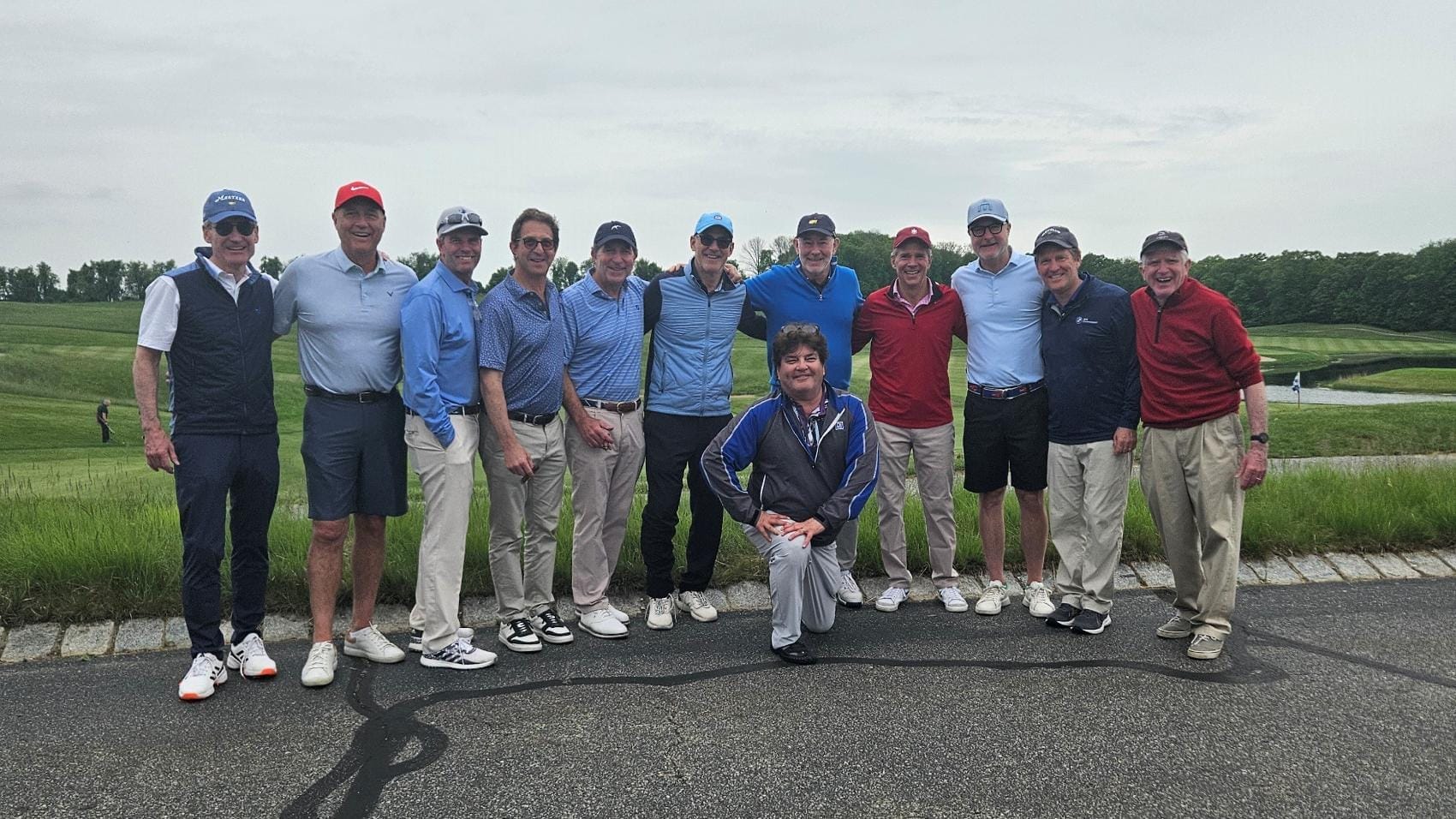 A dozen alumni stand in front of a golf course.