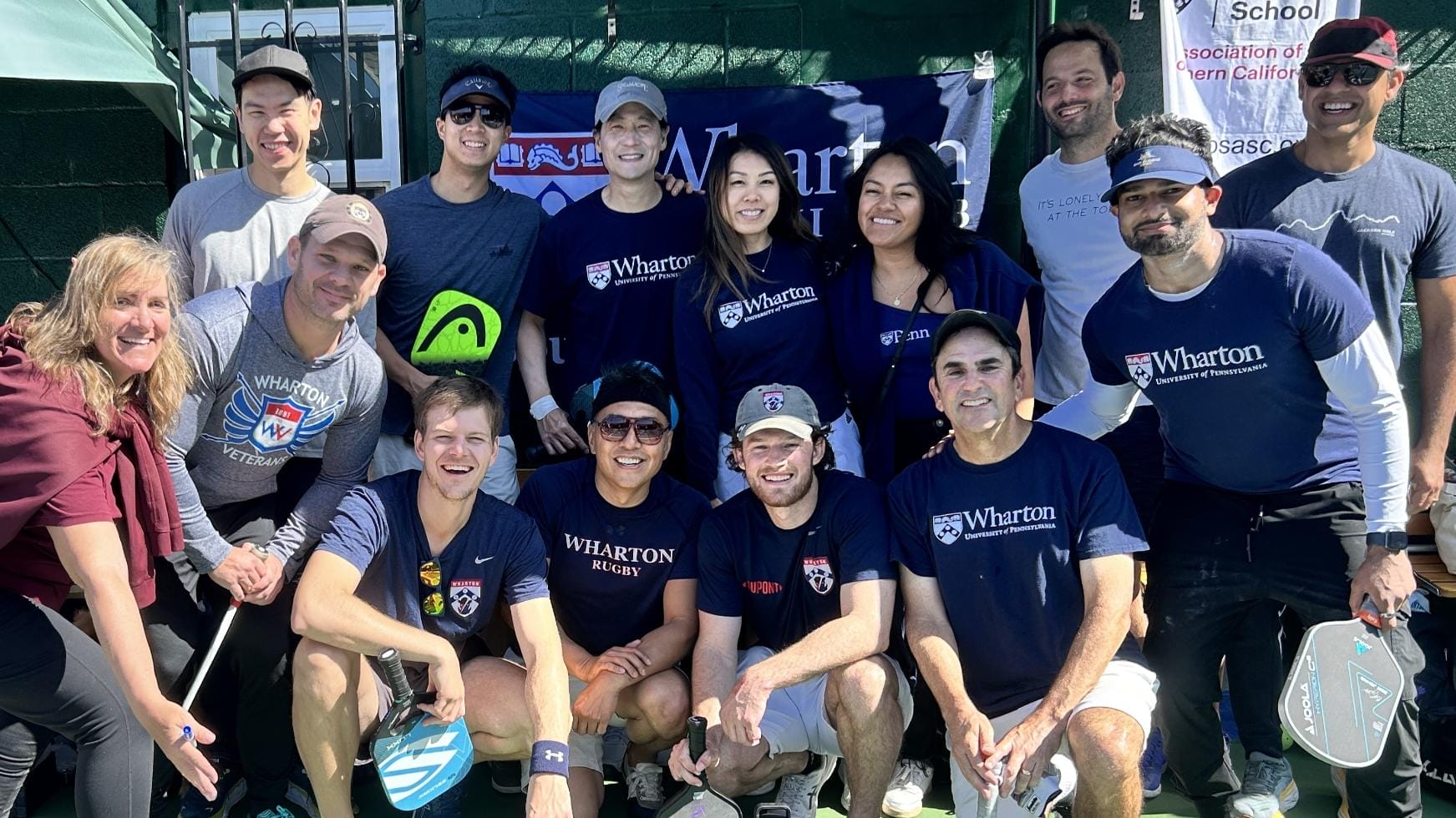 Thirteen people sporting Wharton apparel pose for a photo on a pickleball court.