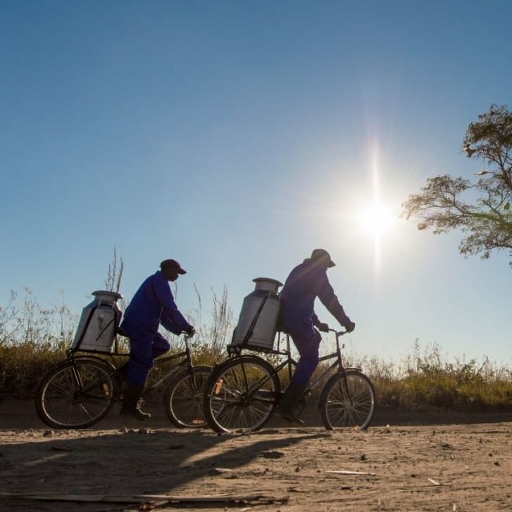 Two men carrying containers on bikes in the desert.