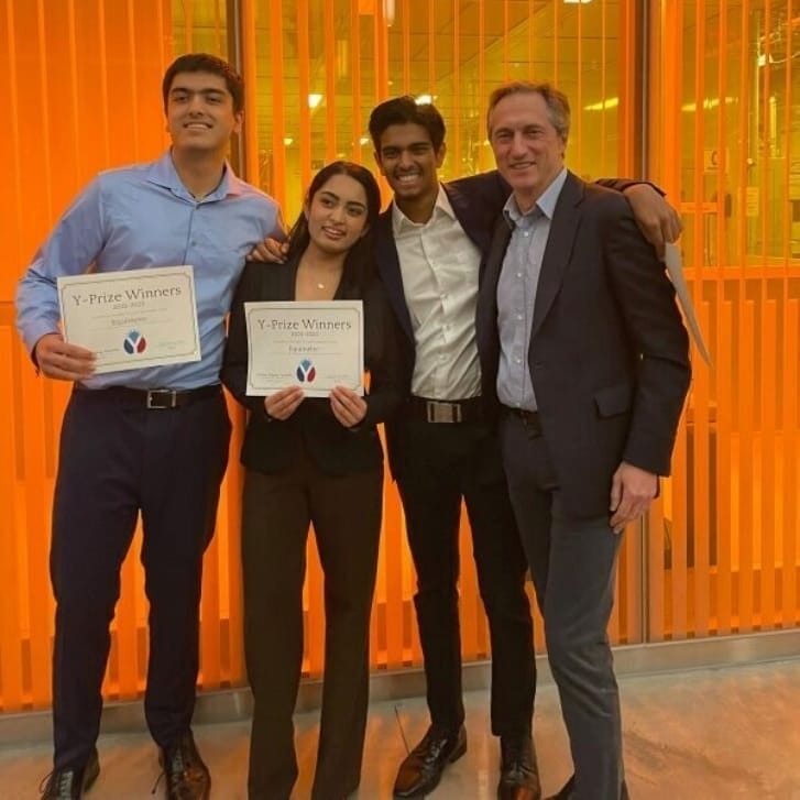 Three students and the executive director of the Mack Institute pose together smiling, with two of the students holding paper awards.