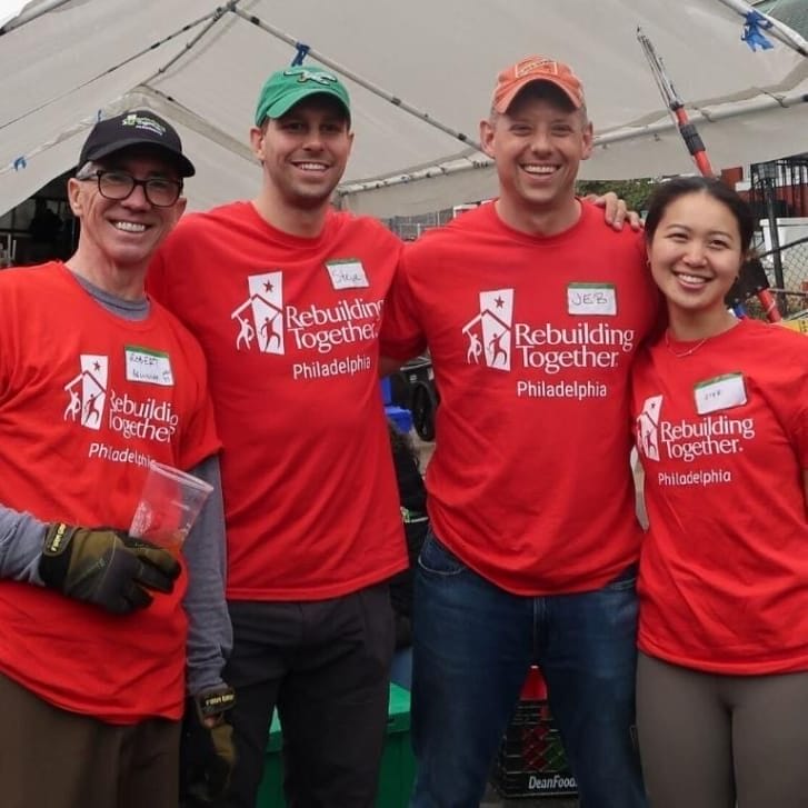 Four people wearing shirts for Rebuilding Together Philadelphia and on-site in a Philadelphia neighborhood for one of the organization's initiatives.