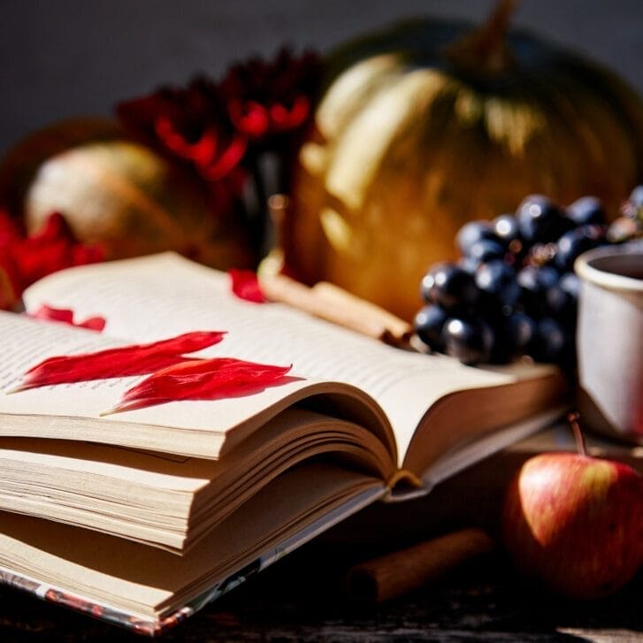 An open book surrounded by fall items such as an apple and a pumpkin.