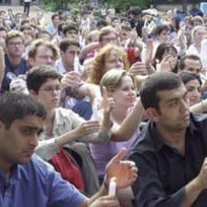 A crowd of people hold candles up outside.