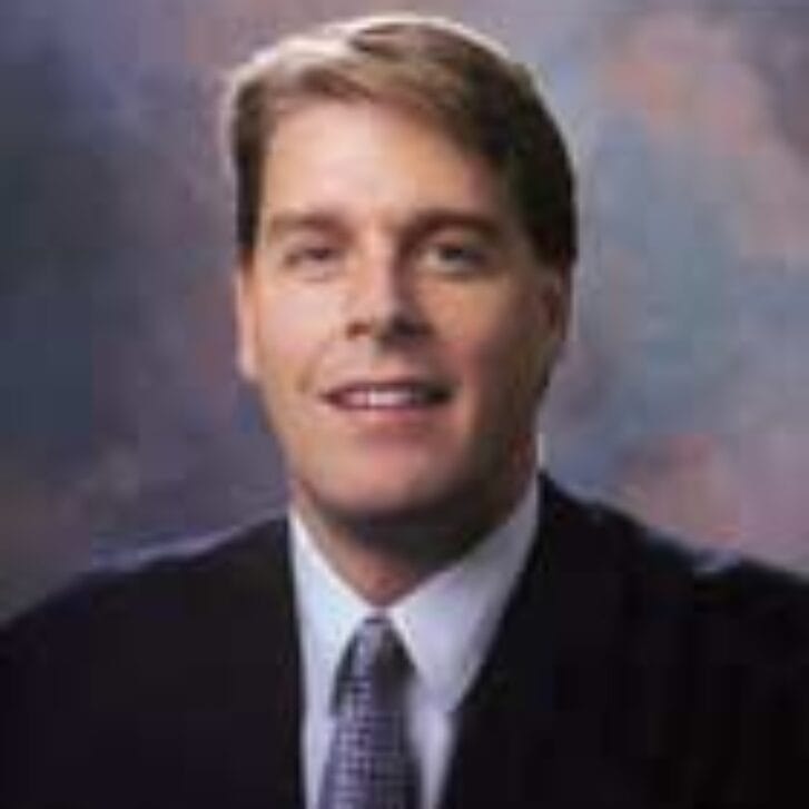 Man smiles in a suit and blue tie.