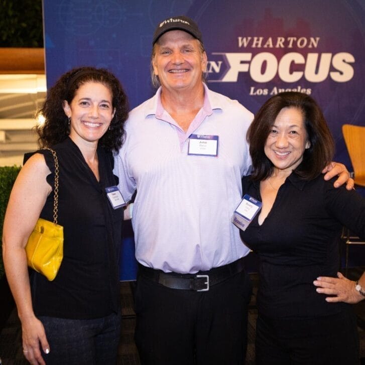 Three alumni in business casual clothing stand in front of a backdrop with the words 